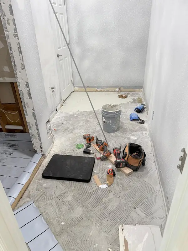 Bathroom floor during preparation, with fresh thinset trowel marks, a bucket and tools