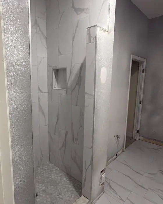 After: finished walk-in shower with marble-look porcelain wall tile, a recessed niche and a round mosaic floor