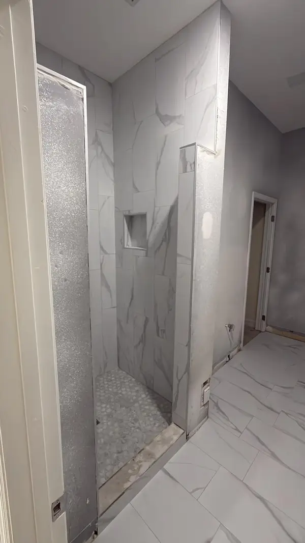 Finished walk-in shower with marble-look porcelain wall tile, a recessed niche and a round mosaic floor beside a large-format tile bathroom floor