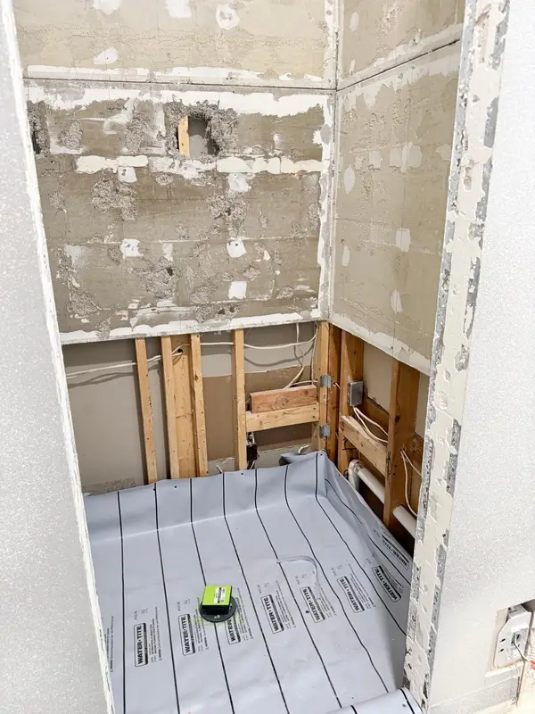 Shower stripped to bare studs and backer board with a gray waterproofing membrane laid on the shower floor