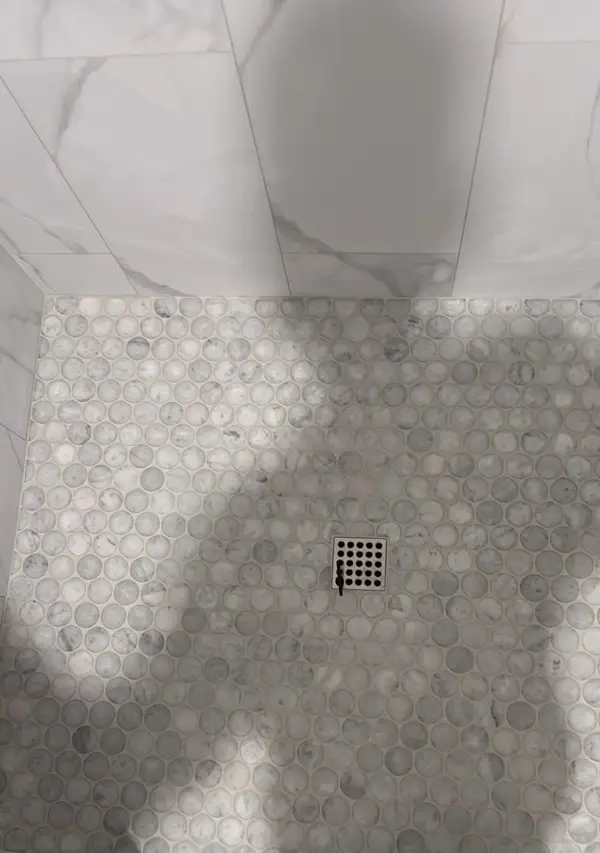 Close-up of a round marble mosaic shower floor with a square stainless drain